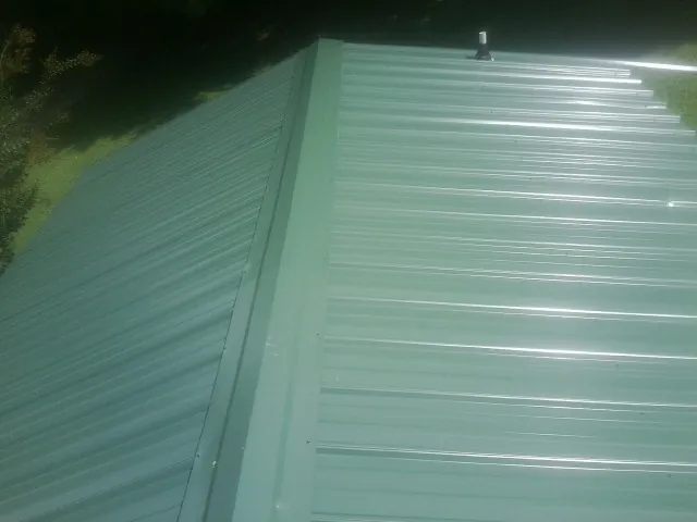 New green metal panels meeting at the ridge of a roof — Flat Roof Repair work by our crew in Mendon